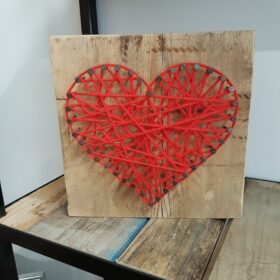 Ein Herz aus Nägeln von einer Palette und Wolle auf Holz vom Baugerüst